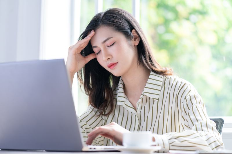 デスクワーク中に頭を押さえる女性